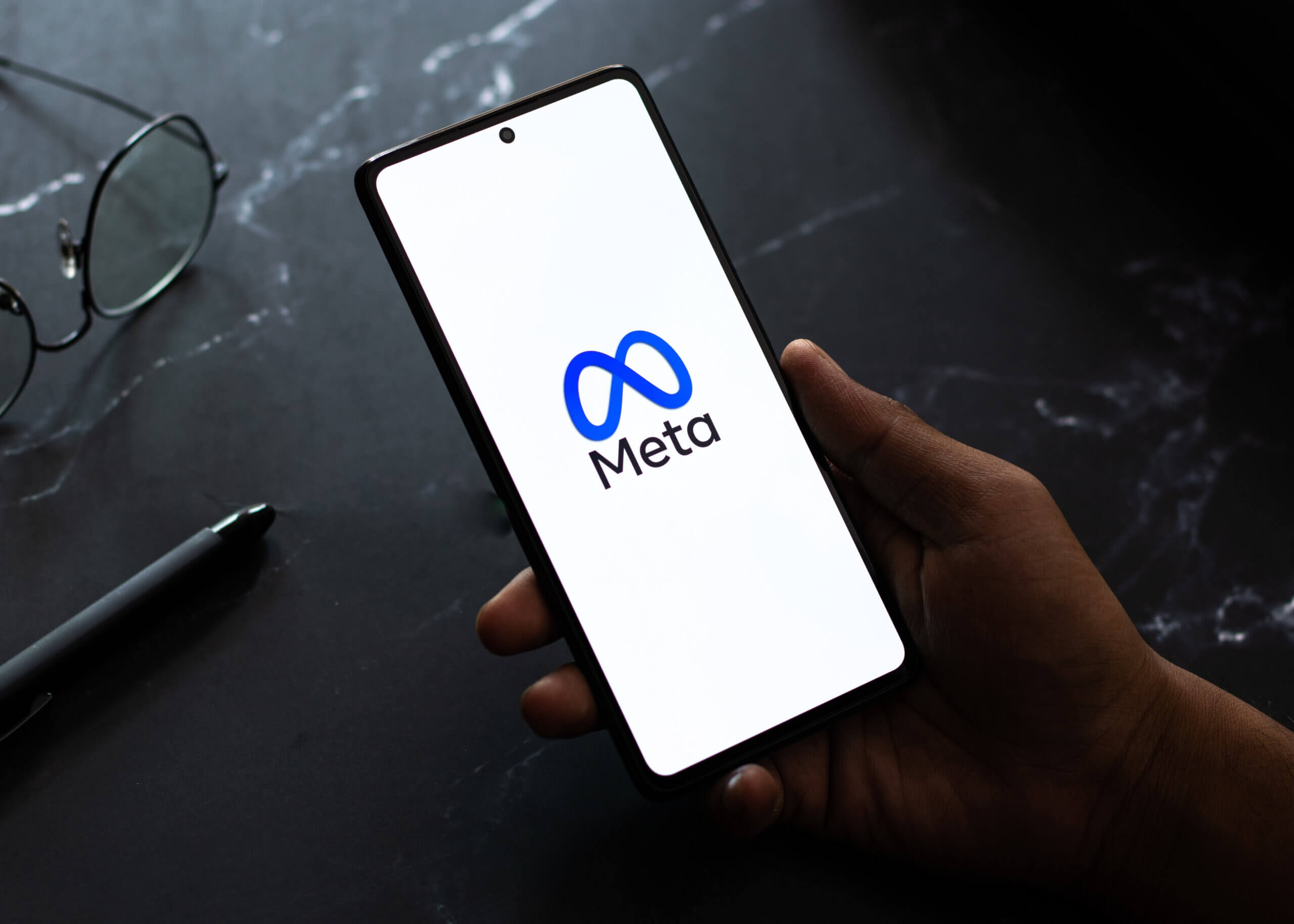 Meta logo on mobile phone which is sat on a black desk.