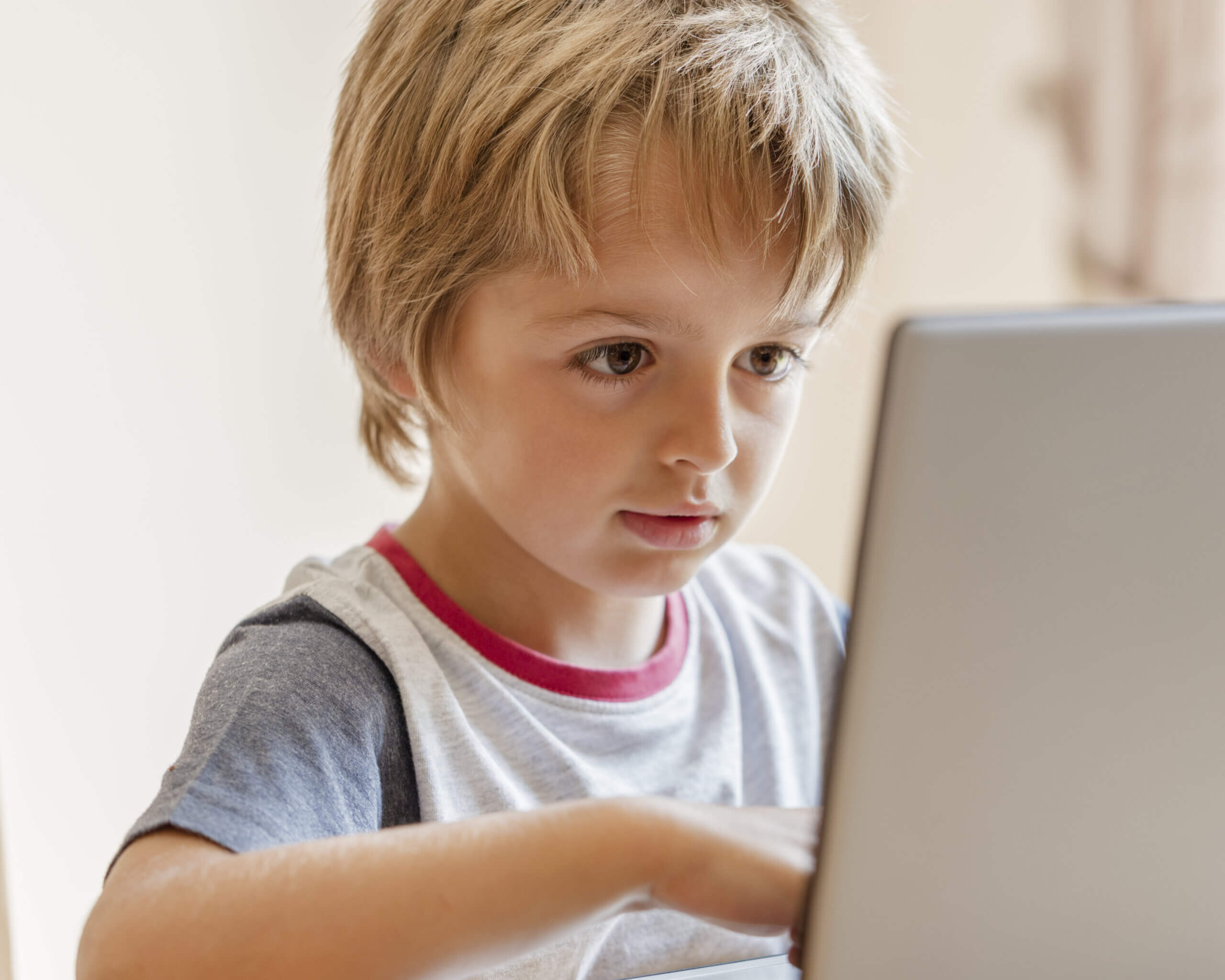 A boy wit blonde hair sits in front of a laptop.