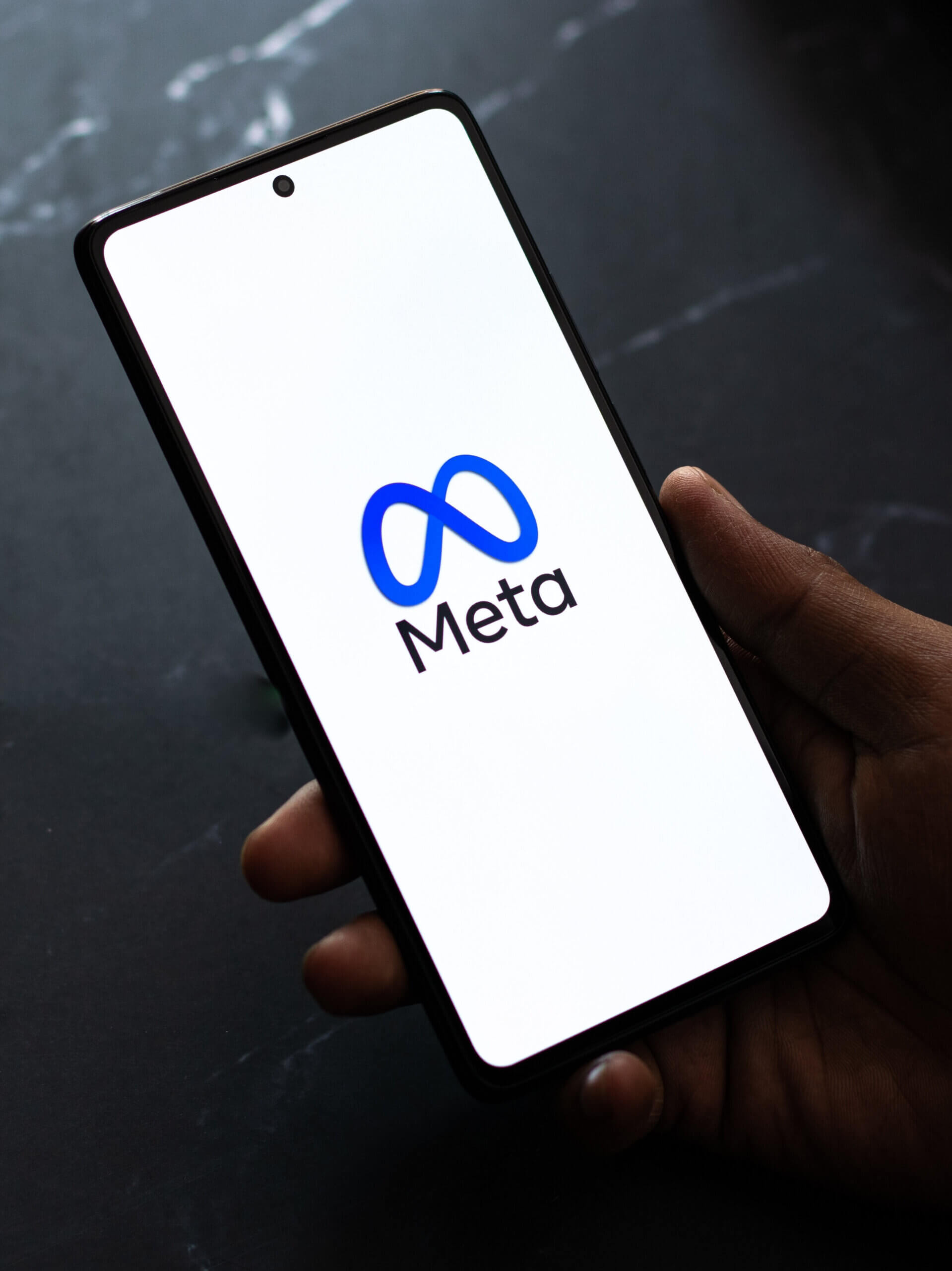 Meta logo on mobile phone which is sat on a black desk.